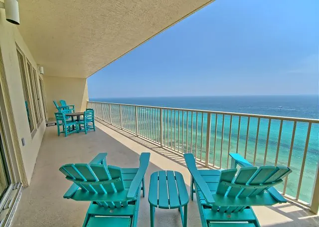 Teal Adirondack chairs on a high-floor balcony overlooking the beach and the Gulf of Mexico