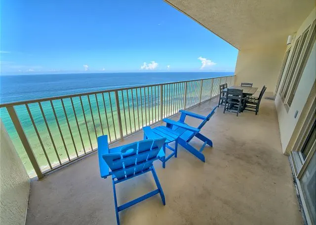 Blue chairs on a Gulf Crest balcony overlooking emerald water and white sand