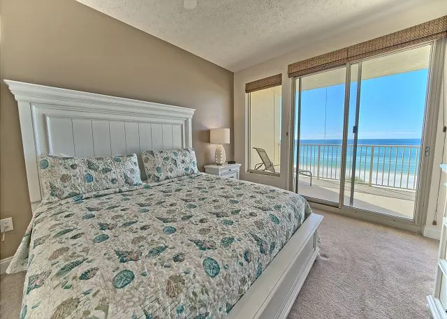 Bright bedroom with a white headboard and sliding doors to an ocean-view balcony