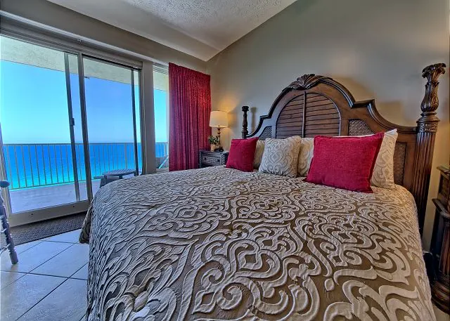 Bedroom with a carved headboard and floor-to-ceiling windows facing the beach and Gulf