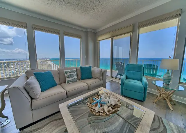 Condo living room with teal armchairs and wraparound windows looking out on the Gulf
