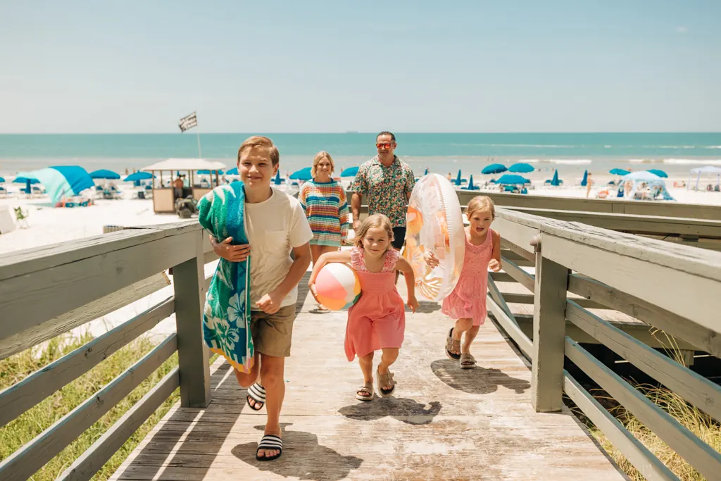Family with beach toys walking up the boardwalk from the beach at Gulf Crest Condominiums
