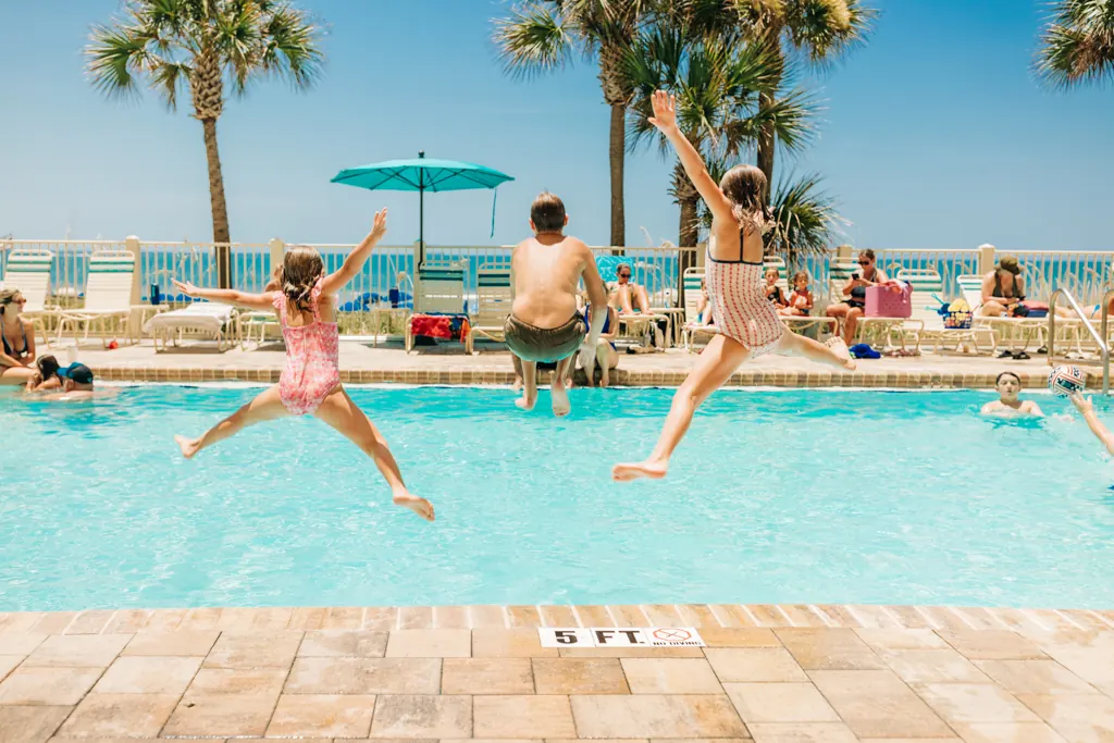 Girl leaping into the pool with palms and umbrellas behind