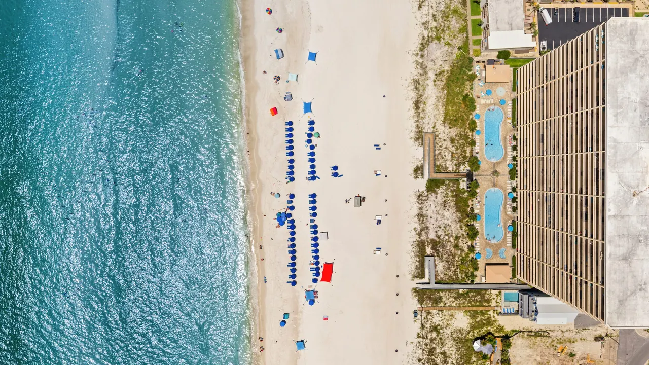 Aerial view of Gulf Crest Condominiums with its two pools, the beach with blue umbrellas, and the Gulf of Mexico