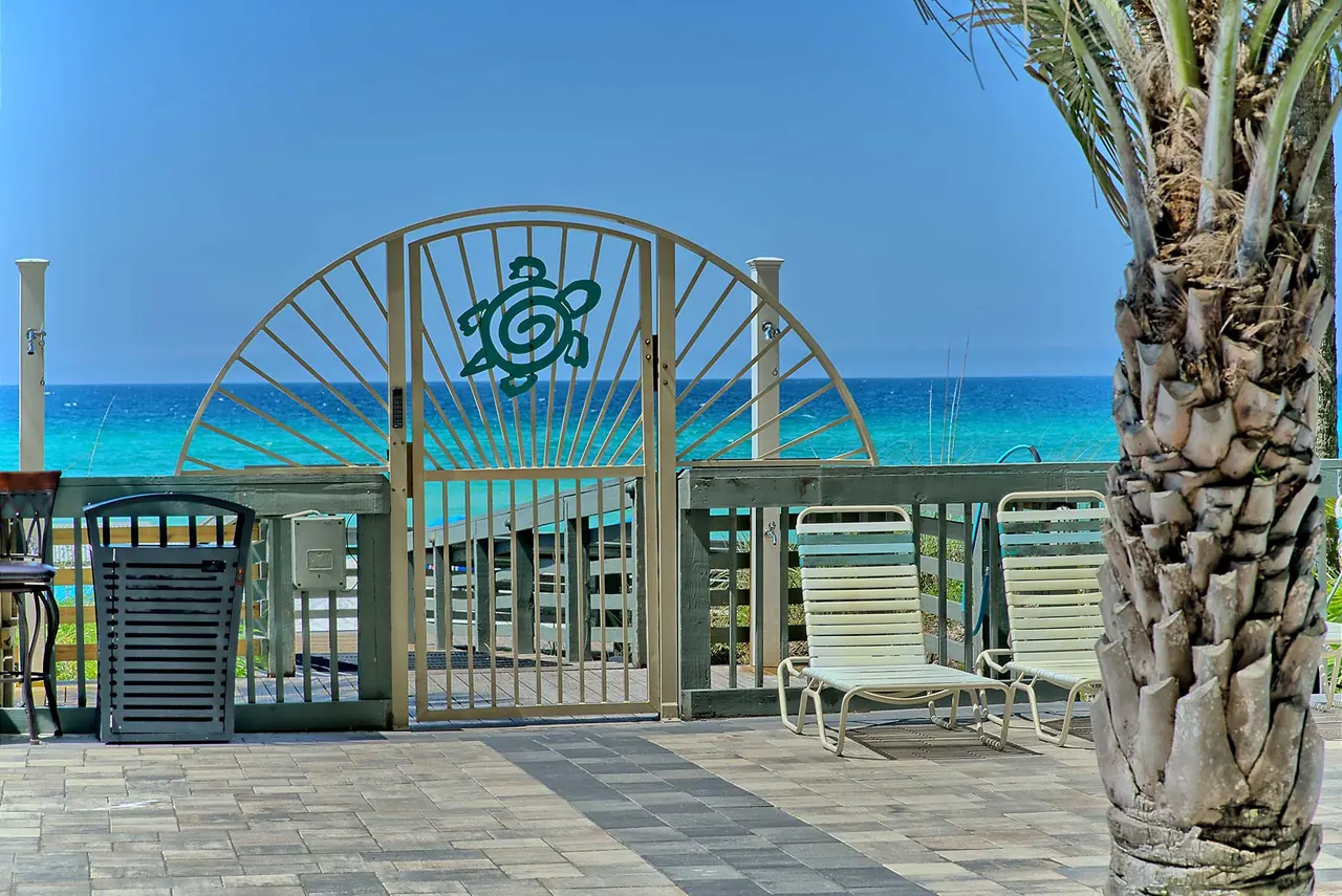 Gate to the beach walkway framed by palm trees, with the Gulf beyond