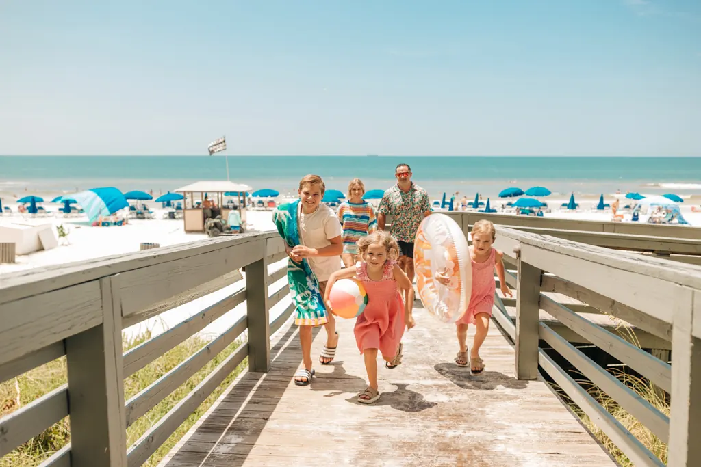 Kids with floats running up the beach boardwalk ahead of their parents