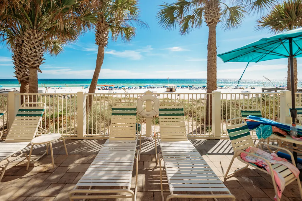 Lounge chairs lined up on the deck with the Gulf and palm trees ahead