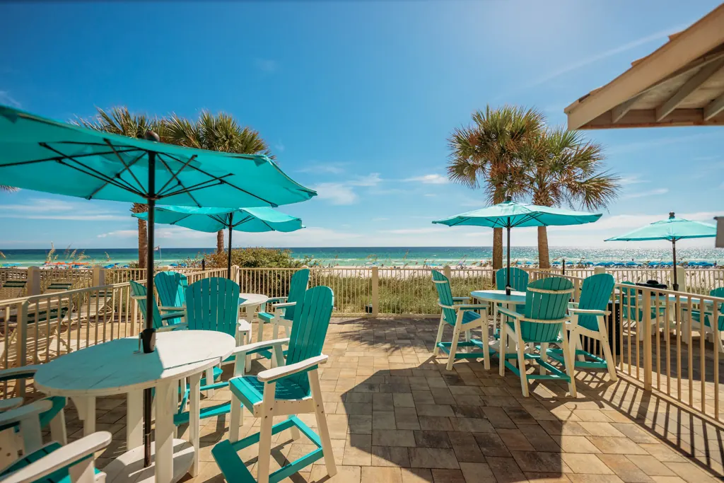 Pool deck tables and teal umbrellas facing the Gulf