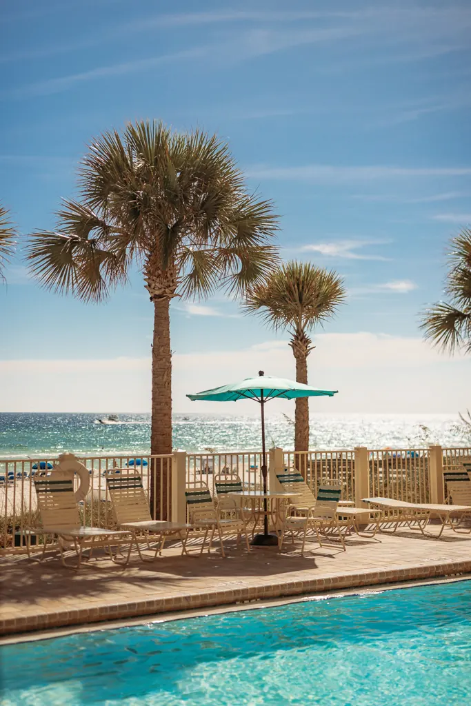 Pool, palm trees and a teal umbrella with the beach behind
