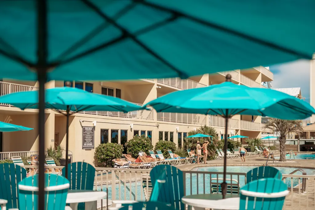 Teal umbrellas and tables on the pool deck below the tower