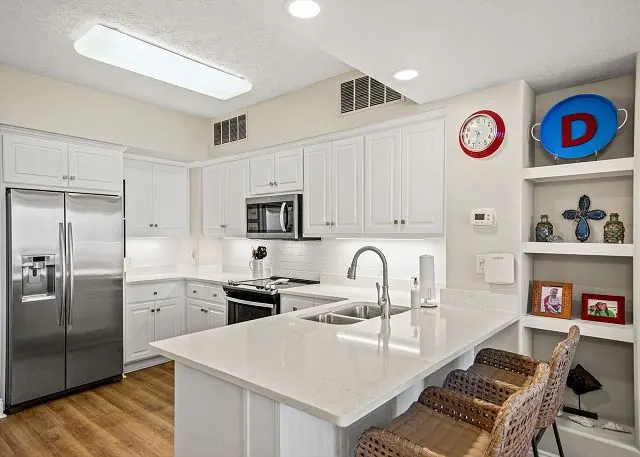 White condo kitchen with a breakfast bar, stainless appliances and pendant lights